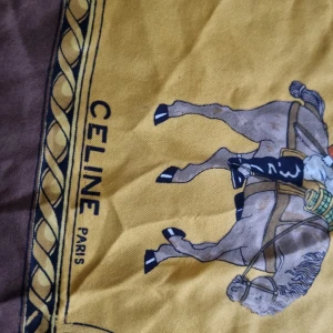 Brun och gul scarf från Celine - V8ntage silkes scarf från Celine med ett klassiskt motiv av hästar och vagnar i brunt och gult. Scarfen har detaljerade illustrationer och text i mitten. Silke.(äkta)