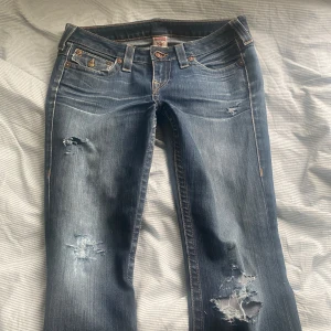 Snygg Blå lågmidjade Bootcut Flared Ripped jeans från True Religion - Säljer ett par blå jeans från True Religion med slitna detaljer. Super cute ripped low waisted true religion bootcut jeans from true religion💓Id say the size is S-M🌟The recent owner has sewn some fabric on the crotch of the pants but its sewn so well that u cant even see it on the outside so it doesnt make a difference💓 Other than that the jeans are in very good condition💗