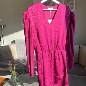 Ny & Other Stories fuchsia klänning - •Snygg fuchsia klänning med subtilt leopardmönster och v-ringning.  •Klänningen har långa ärmar, ett elastiskt band i midjan och en omlott-design som ger en elegant touch. Perfekt för att sticka ut med stil! •Ny med etiketten kvar. Lite mindre i storleken, passar bättre till 42.  •Köpte för 790 kr. •Djur&rökfritt hem
