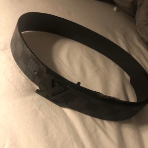 Rutig bälte med monogramspänne - Snyggt bälte med rutigt mönster och ett stilrent monogramspänne. Perfekt för att ge din outfit en extra touch. Passar bra till både jeans och kostymbyxor.