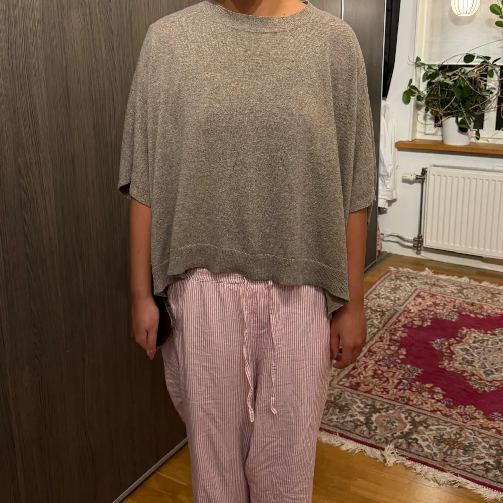 Säljer en mysig beige stickad poncho med en lös passform. Perfekt för kyliga dagar och ger en avslappnad stil. Den har en enkel design med ribbade kanter.. Neuletakit & Villapaidat.