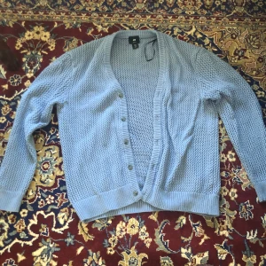 Ljusblå kofta från H&M - Säljer en ljusblå kofta från H&M med en luftig stickad design. Koftan har en loose fit och knappar framtill. Perfekt för en avslappnad stil.