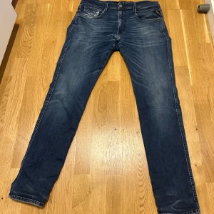 Replay anbass  - Snygga blå jeans från Replay i modellen Hyperflex Anbass. De har en klassisk femficksdesign och en knappgylf. Perfekta för en stilren look. Jenssen har några slitage och defekter dessa syns dock på vissa av bilderna