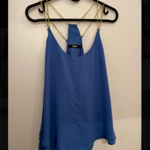 Blå ärmlös topp från BikBok  - Snygg blå ärmlös topp från BikBok med tunna guldiga kedjeband. Toppen har en lös passform och är tillverkad i ett lätt och luftigt material.