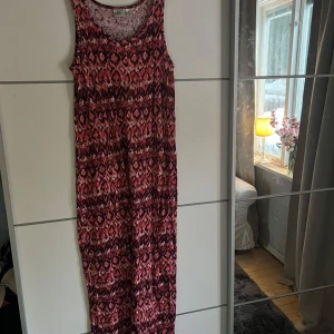 Mönstrad långklänning från Isolde - Säljer en färgglad långklänning från Isolde med ett unikt mönster i rosa och vinröda toner. Klänningen är ärmlös och perfekt för sommarens varma dagar. Den har en bekväm passform och är tillverkad i ett mjukt material.