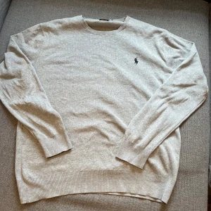  Polo Ralph Lauren tröja - Säljer en stilren grå tröja från Polo Ralph Lauren i Pima bomull. Tröjan har en broderad logga på bröstet och är slim fit. Perfekt för en klassisk och avslappnad look.