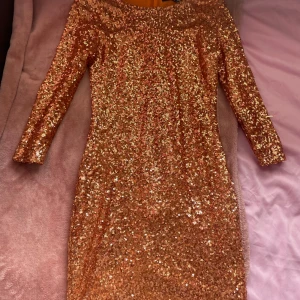 Glittrig klänning från TFNC London - Säljer en glittrig klänning från TFNC London i en vacker guldton. Klänningen har trekvartsärmar och en dragkedja i ryggen för enkel påklädning. Perfekt för att glänsa på festen! ✨