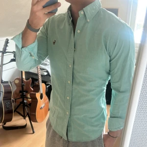 Grön skjorta med broderad logotyp - Snygg ljusgrön skjorta från Ralph Lauren med en broderad logotyp på bröstet. Skjortan har långa ärmar och knappar framtill samt vid kragen. Perfekt för en stilren look.