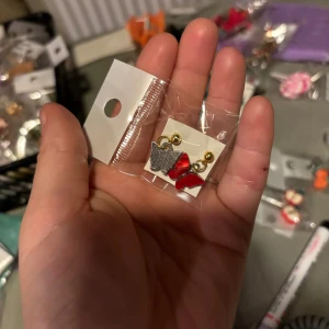 Söta örhängen med röda rosetter - Charmiga örhängen med små röda rosetter och guldfärgade detaljer. Perfekta för att lägga till en lekfull touch till din outfit. De är lätta och bekväma att bära hela dagen.