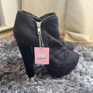 Svarta boots med dragkedja - Snygga svarta boots från Wildflower med hög klack och dragkedja på sidan. Skorna har en rundad tå och är tillverkade i ett syntetmaterial. Perfekta för att ge lite extra höjd och stil till din outfit.