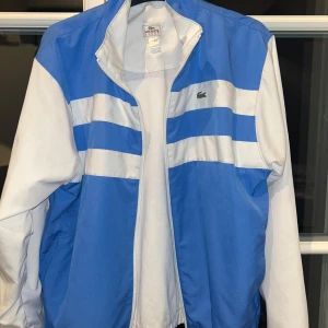 Lacoste tracksuit  - Super snygg lacoste tracksuit i ljusblå/vit med matchande ljusblåa byxor. Lacoste tryck på ryggen och logotyp på dragkedjan. Inga tecken på användning. Storlek 164 men när jag köpte den stod det att det passar xs också och jag som är 170 och har xs den passar bra. Köpte den för ungefär 2000kr från en tysk hemsida då den inte säljs längre