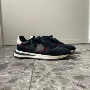 Mörkblåa sneakers från Philippe Model - Hej, jag säljer mina snygga mörkblåa sneakers från Philippe Model med röda och grå detaljer. Skorna är i storlek 44, skorna är knappt använda. Jag fick betala 2700kr nypris för dessa och jag säljer dom för 2200kr, hör av er för fler frågor!