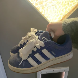 Blå Adidas Campus sneakers - Snygga blå Adidas Campus sneakers med vita ränder och snörning. Perfekta för en avslappnad stil. Skorna har en klassisk design med en väldigt bekväm sula. Använda en halv sommar, pris kan diskuteras via snabbköp. Blåa snören hänger me (helt oanvända)