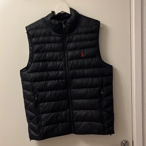 Blå dunväst från Polo Ralph Lauren - Snygg mörkblå dunväst från Polo Ralph Lauren i nyskick. Köpt som ny för två månder sedan och väldigt sparsamt använt. 