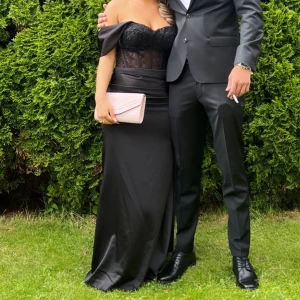 Svart balklänning  - Elegant svart långklänning med spetsdetaljer och axelbandslös design. Klänningen har en figurnära passform med en vacker slits och omlott-effekt. Klänningen har använts bara en gång, vilket var på balen. Den har även kemtvättats i Stockholm så det är gott som ny! Köpt för 2000kr i butik ❤️