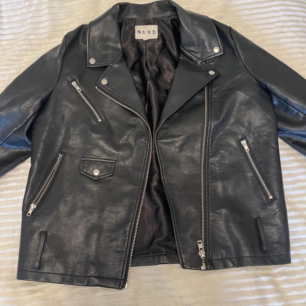 Snygg svart skinnjacka från NA-KD med flera dragkedjor och en klassisk bikerstil. Jackan har en asymmetrisk dragkedja framtill och två snedställda fickor med dragkedjor. Super snyggt över stickade tröjor! 💕. Takit.