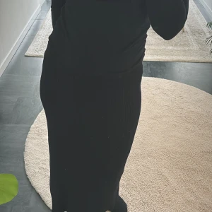 Svart ribbad långkjol - Snygg svart ribbad långkjol som passar perfekt till både vardag och fest. Kjolen har en elegant slits och är gjord i ett mjukt och stretchigt material för bästa komfort. Perfekt för höst och vinter!