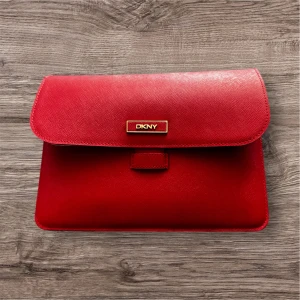 Röd laptopfodral  från DKNY - Snygg röd laptopfodral  från DKNY med elegant guldfärgad logotyp på framsidan. Kan använda också för att bära dina viktigaste tillhörigheter. Insidan är fodrad med ett mönstrat tyg och har plats för både pass och mobil.