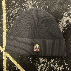 Svart stickad mössa från Parajumpers - Snygg svart stickad mössa från Parajumpers med ribbad kant och ett broderat märke framtill. Perfekt för kyliga dagar och en stilren look.
