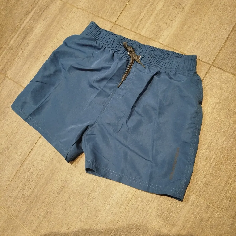 Säljer ett par blå badshorts från Aquawave. De har en elastisk midja med snörning och en praktisk bakficka. Perfekta för sommarens badäventyr! 🏖️ Inköpta på badhuset för 299 kr i December och sedan endast upptvättade. Står 16 år i dom och är som ett par xs. . Shortsit.