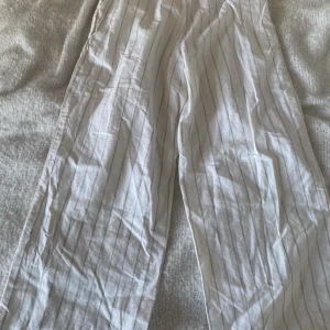 Vita randiga linnebyxor - Säljer ett par vita byxor med tunna ränder. Linnebyxorna är nästan aldrig använda. Inga hål.inga fläckar. De är tillverkade i ett lätt material som passar bra för varmare väder. 