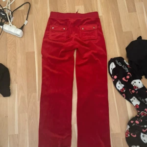 Röda byxor från Juicy Couture - Snygga röda byxor från Juicy Couture i mjukt material. De har en tight passform och är perfekta för en avslappnad stil. Byxorna har en elastisk midja med snörning och bakfickor med knappar. Använd 1 gång, jätte bra skick och original priset är 1200kr ❤️