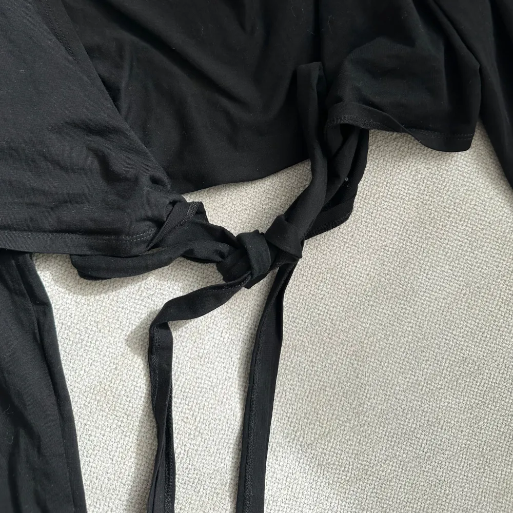 Snygg svart knytblus med långa ärmar och en stilren design. Perfekt för att lägga till en touch av elegans till din outfit. Blusen har en knytning framtill som ger en fin detalj.. Yläosat.