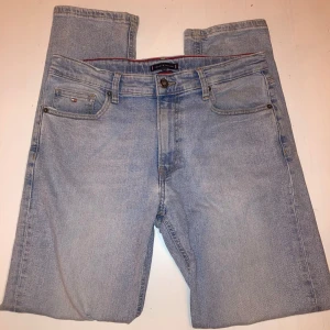 Ljusblå jeans från Tommy Hilfiger - Snygga ljusblå jeans från Tommy Hilfiger med klassisk femficksdesign och knappgylf. Perfekta för en avslappnad stil. Märkets logotyp syns på den lilla fickan och insidan av midjan🌟