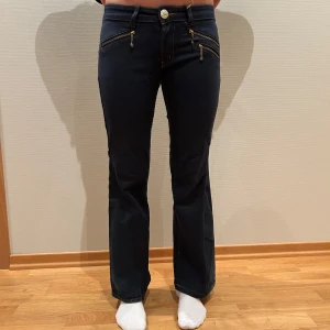 Mörkblå bootcut jeans med dragkedjor - Snygga mörkblå bootcut jeans med dekorativa dragkedjor framtill. Byxorna har en låg midja och en klassisk femficksdesign.                        Omsydda jeans Lågmidjade bootcut  Grenmått: 18 cm Midjemått: 33 cm Innerbenslängd: 72 cm