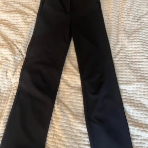 Svarta kostymbyxor från Vero Moda - Snygga svarta kostymbyxor från Vero Moda med en klassisk design. Byxorna har en dragkedja och knapp framtill samt hällor för bälte. Perfekta för en stilren look.