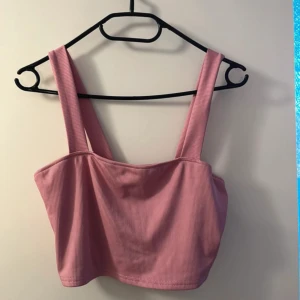 Rosa ribbad linnetopp - Säljer en söt rosa ribbad linnetopp med breda axelband. Toppen är croppad och perfekt för varma dagar. Den har en enkel och stilren design som gör den lätt att matcha med olika outfits.
