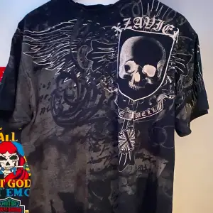 Cool svart t-shirt från Xzavier med ett stort dödskallemotiv och vingar på framsidan. Texten 'Libertas' och 'We Will' ger en edgy känsla. Perfekt för dig som gillar en rockig stil.