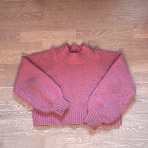 Rosa stickad tröja från Gina tricot - Säljer en mysig rosa stickad tröja från Gina tricot. Tröjan har en hög ribbad krage och långa ärmar med ribbade muddar. Perfekt för kyliga dagar och ger en trendig look. Passar bra till både jeans och kjol. Den är en magtröja.