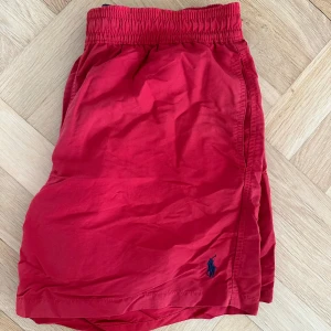Röda badbyxor från Ralph Lauren - Snygga röda badbyxor från Ralph Lauren med elastisk midja och den klassiska loggan broderad i blått. 