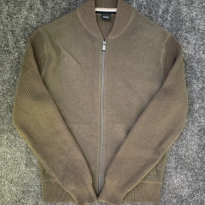 Stickad cardigan  - Sjukt fet stickad cardigan från Hugo Boss i storlek S. Sjukt snygga ribbade armar. Nypris runt 3000kr, mitt pris endast 795kr. Skicket är som ny. Riktigt snygg brun/grön färg
