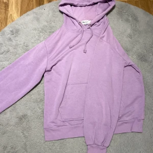 Lila hoodie från NA-KD - Säljer en snygg lila hoodie från NA-KD. Den har en klassisk design med en stor ficka framtill och justerbar huva med dragsko. 