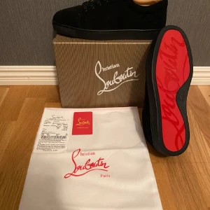 Svarta sneakers från Christian Louboutin - Snygga svarta sneakers från Christian Louboutin med ikonisk röd sula och nitar på tån. Skorna har en stilren design med snörning och är tillverkade i mocka. Perfekta för att ge din outfit en lyxig touch.