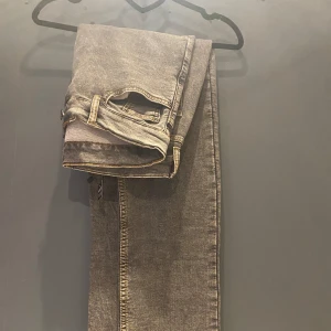 Grå jeans från Monten - Snygga grå jeans från Monten med klassisk femficksdesign och knappgylf. De har en rak passform och är perfekta för en avslappnad stil. Jeansen har dekorativa sömmar på bakfickorna.