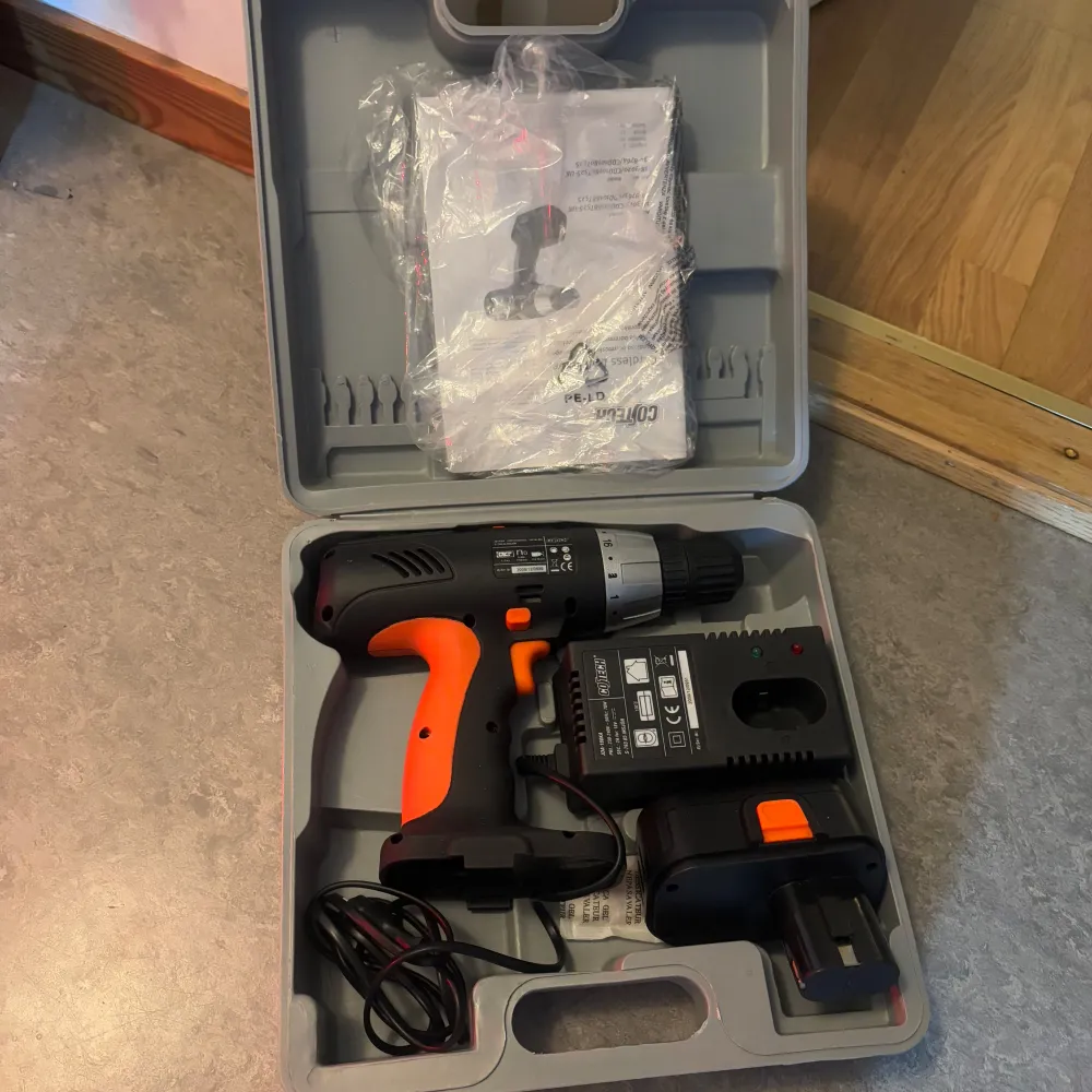 Praktisk borrmaskin i en grå plastväska med orange och svart design. Inkluderar laddare och batteri samt manual. Perfekt för hemmafixaren som behöver ett pålitligt verktyg för diverse projekt.. Böcker.