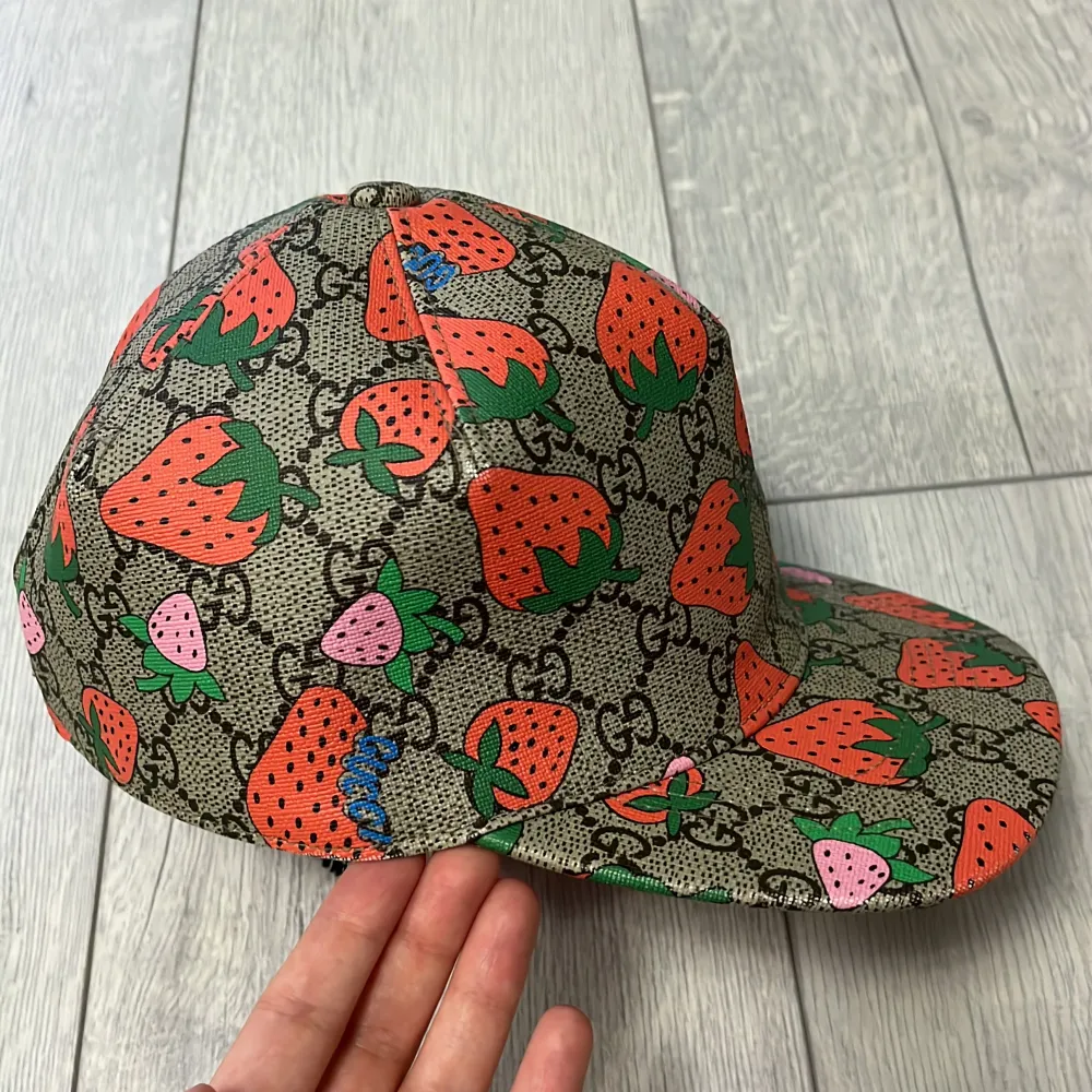 Snygg keps från Gucci med ett lekfullt jordgubbsmönster i rött och grönt på en beige bakgrund. Kepsen har en justerbar rem i rosa på baksidan och en rosa insida. Perfekt för att ge din outfit en färgglad touch!. Asusteet.