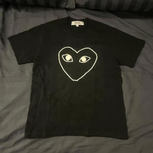 Comme des Garçons T-shirt  - En riktig snygg svart T-shirt från Comme des Garçons. Med en vit logga på framsidan av tröjan på bröstet. | Den är så gott som ny i skicket 9,5/10. | Det är bara att höra av sig om man har några frågor🕺🏻🕺🏻🕺🏻
