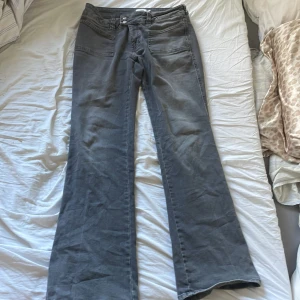 Grå bootcut jeans - Snygga grå bootcut jeans med låg midja. De har en klassisk femficksdesign och stängs med dragkedja och knapp. Perfekta för en avslappnad stil.