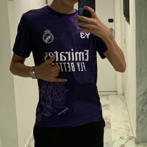 Real Madrid tredje ställ lila tröja - Säljer en snygg lila fotbollströja från Y-3 med ett unikt rosmönster. Den är sällsynt, är riktigt snygg och passar perfekt för sommaren. Den är storlek m men passar s. Den har en fet ucl emblem och väldigt unika färger. Tröjan är också nästan oanvänd. Pris kan diskuteras vid snabba köp.