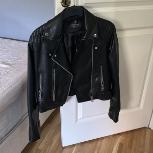 Skinnjacka från Stradivarius - Snygg skinnjacka från Stradivarius med quiltade detaljer på axlarna och metal remmar vid sidan. Jackan har en klassisk bikerstil. Perfekt för en cool look!