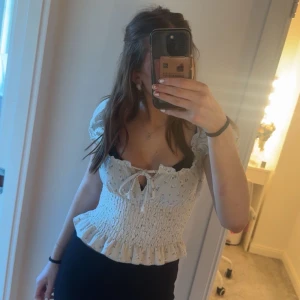 Blommig topp med volangdetaljer - Blommig ljusgrön topp med volangdetaljer och knytning framtill. Toppen har korta ärmar och en smockad midja som ger en fin passform. Perfekt för en somrig look! Toppen är endast använd en gång.