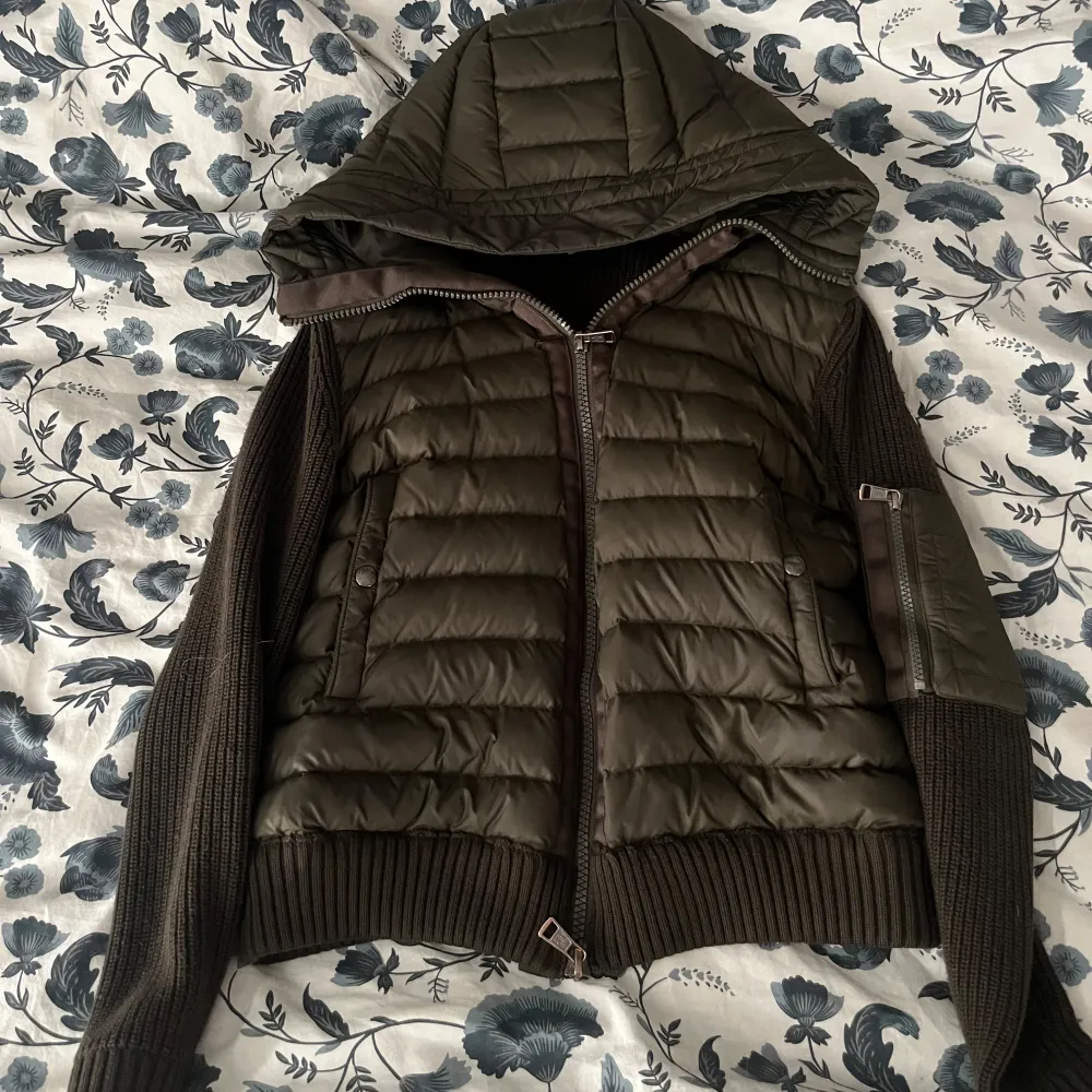 Snygg olivgrön cardigan från Moncler med stickade ärmar och huva. Jackan har dragkedja framtill och ribbade muddar. Perfekt för kyligare dagar.. Takit.