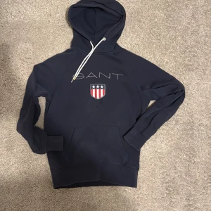 Mörkblå hoodie från GANT - Säljer en snygg mörkblå hoodie från GANT. Riktigt skön tröja som du kan använda när du vill vara hemma en kväll med sköna kläder men även på vardagen.