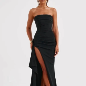 Svart axelbandslös klänning med slits - Elegant svart axelbandslös klänning med en hög slits och draperad design. Perfekt för en kväll ute eller en speciell tillställning.