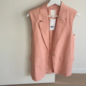 Rosa väst från H&M - Snygg rosa väst från H&M i en stilren design. Västen har en knapp framtill och två fickor. Perfekt för att lägga till en touch av färg till din outfit.