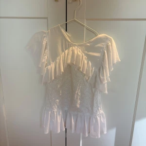 Vit blus med volangdetaljer - Säljer en söt vit blus med volangdetaljer och spetsmönster. Blusen har korta ärmar och en luftig passform🩷